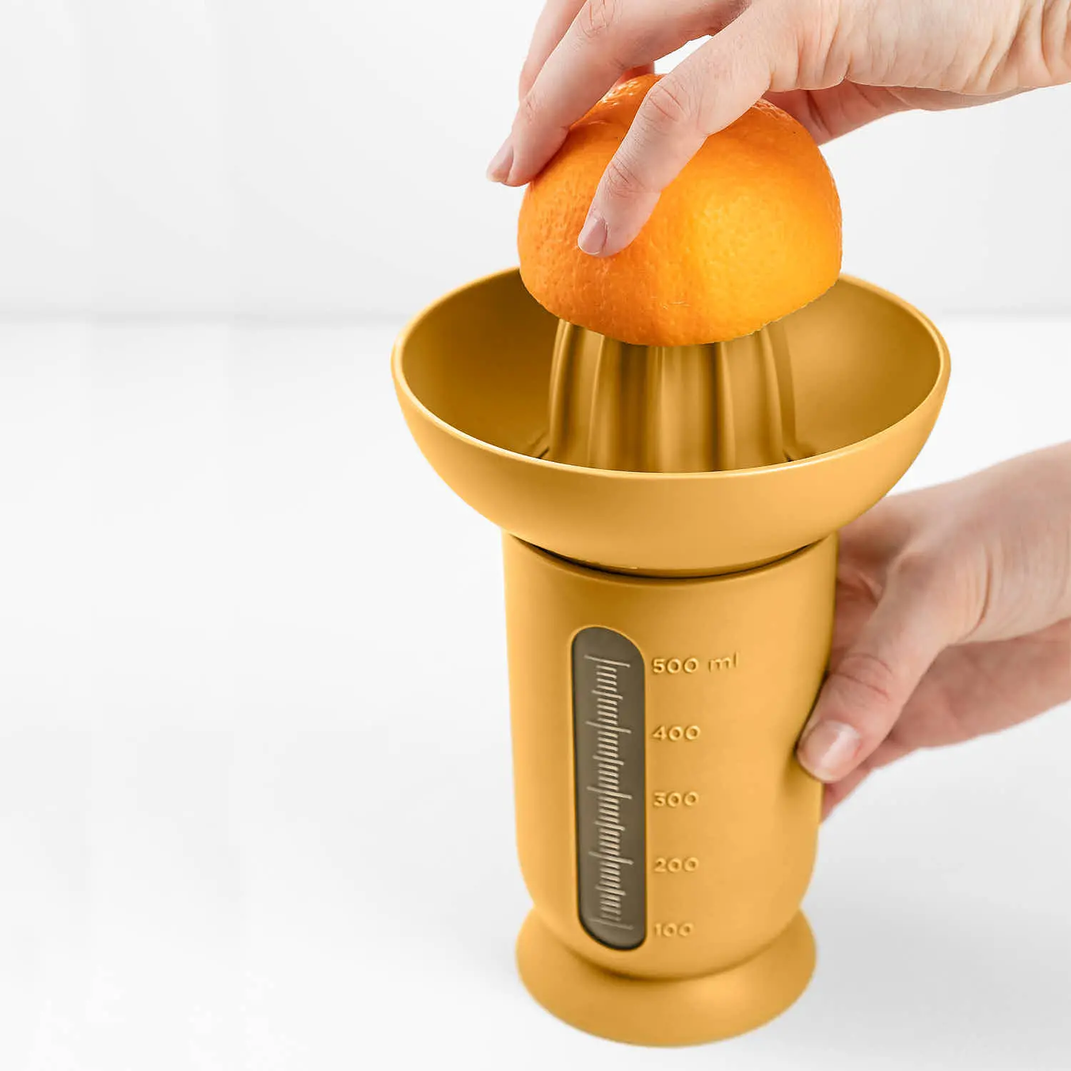 Ufo Blim Plus: person squeezing an orange with the citrus juicer with graduated carafe up to 500 ml in Desert color